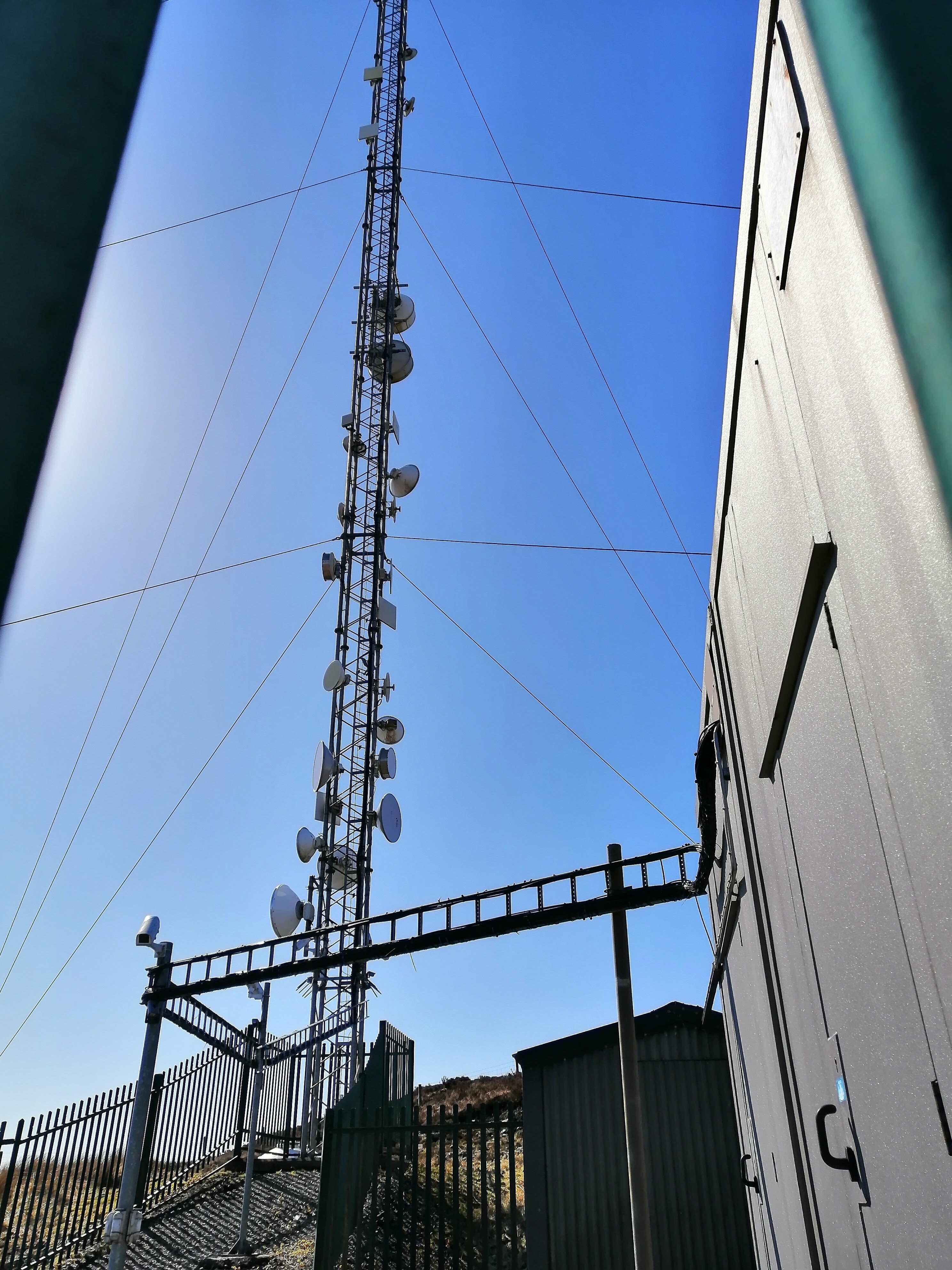 The microwave mast. It has a pre-fab building and a building constrcted from corrugated sheeting at the base within the compund - a vertical cable tray mounted on poles carries cables across the yard from the building to the mast. A number of CCTV cameras are visible inside the compund.
