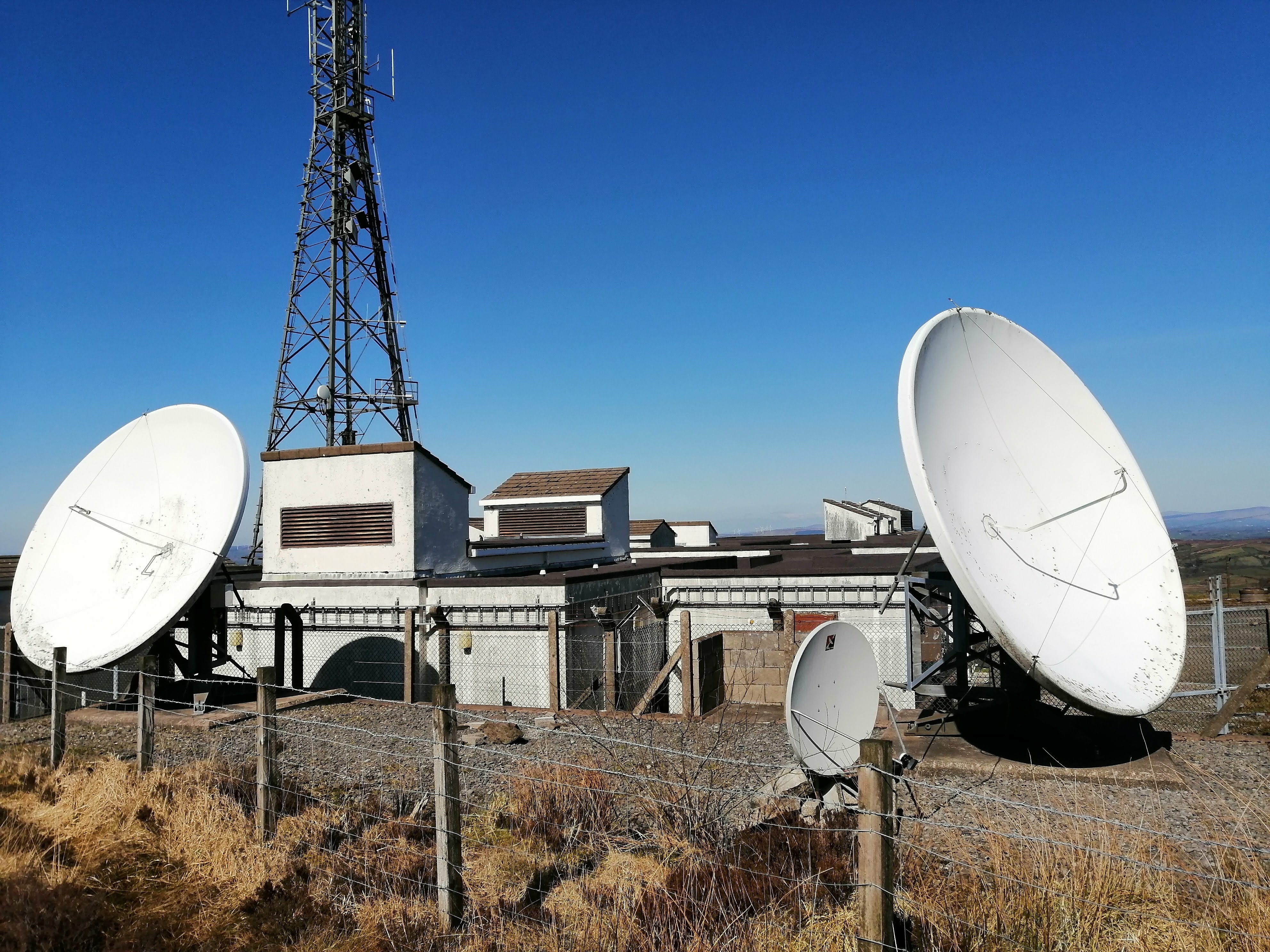 Two very large (~2m diameter) and more standard sized satellite dishes, pointed in different directions. They are attached to large metal stands which are bolted the the concrete floor. These are actually just outside the main compund.