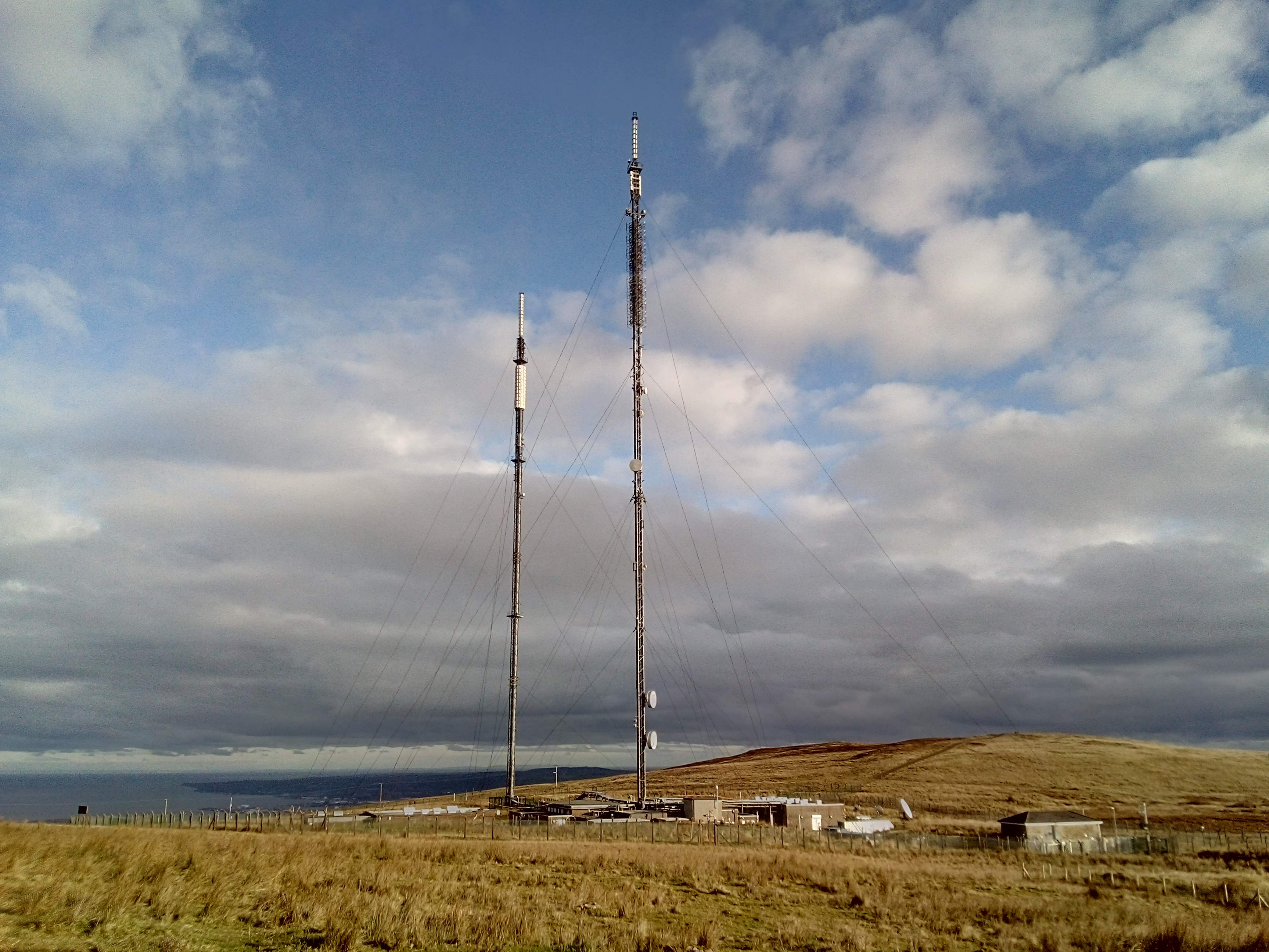 Tall stayed masts of approximately equal height, with large microwave dishes and a sprawling transmitter hall at the base.