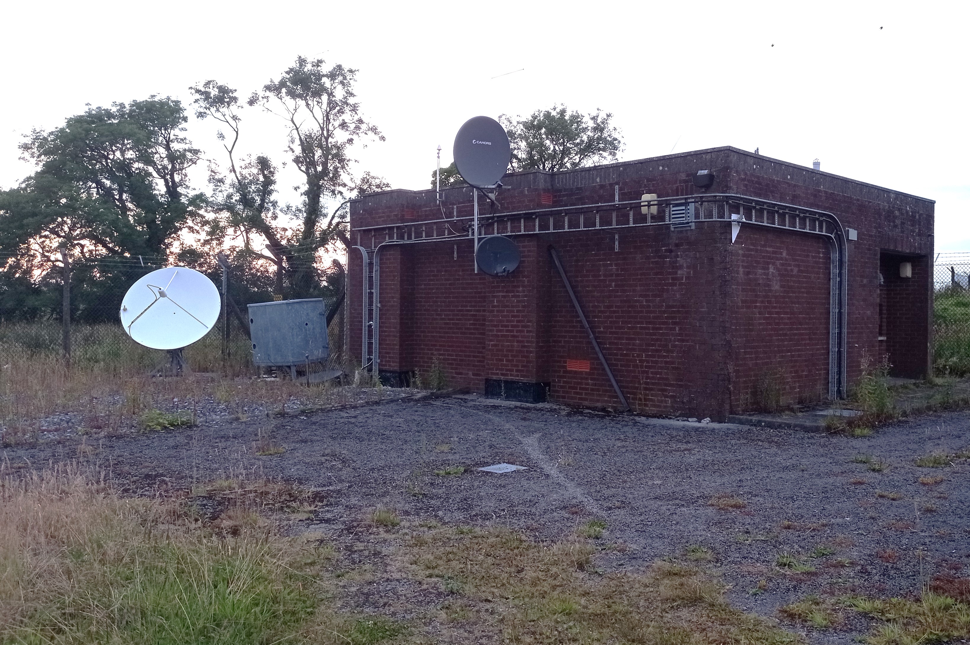 Small red-brick transmitter buildin, featuring three satellite dishes and a GPS timing antenna.