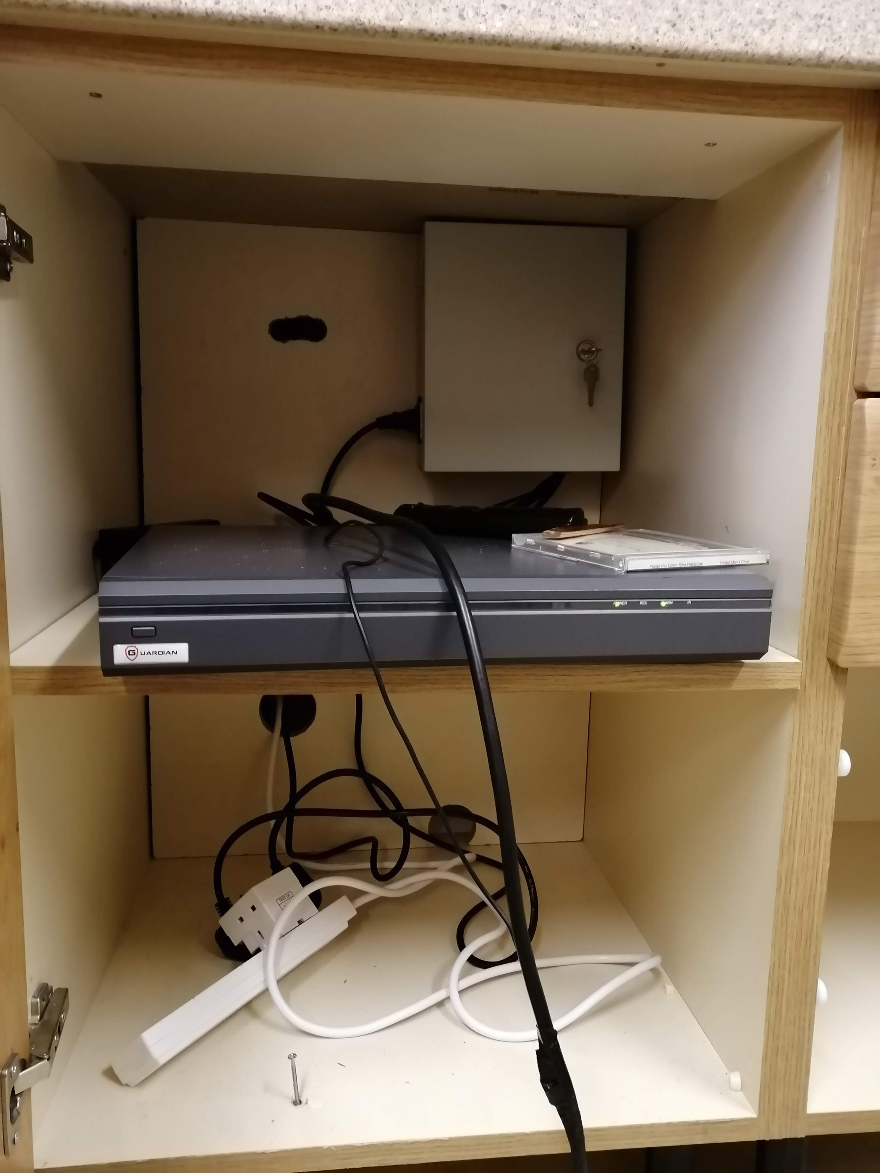 Kitchen built-in cupboard split in two by a shelf. The top shelf contains a CCTV DVR and a locked metal cabinet. The bottom shelf contains a number of cables.